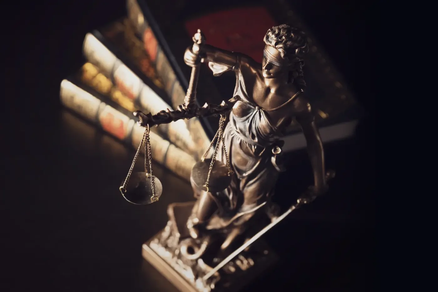 Scales of justice goddess next to three law books against a black background.