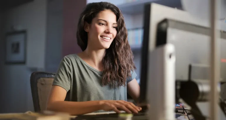 Smiling young woman studying for the bar exam online using Themis Bar Review course on a desktop computer in a home office environment.