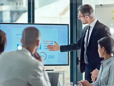 Business professional giving a presentation using bar graphs and data charts to a diverse team in a classroom setting, demonstrating bar exam success statistics.