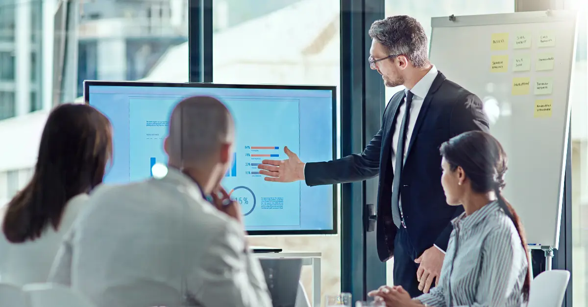 Business professional giving a presentation using bar graphs and data charts to a diverse team in a classroom setting, demonstrating bar exam success statistics.