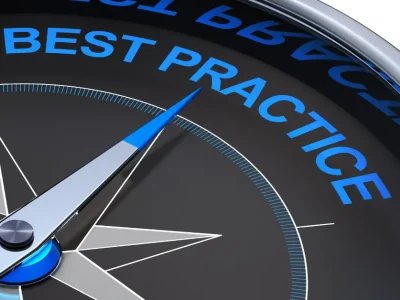 A close-up of a modern metallic compass face with a sleek silver and blue needle pointing toward the words “BEST PRACTICE.”