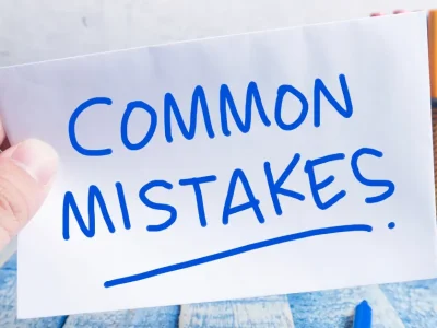A hand holding a paper with the words "COMMON MISTAKES" written in bold blue marker, with colored pencils in a holder in the background.