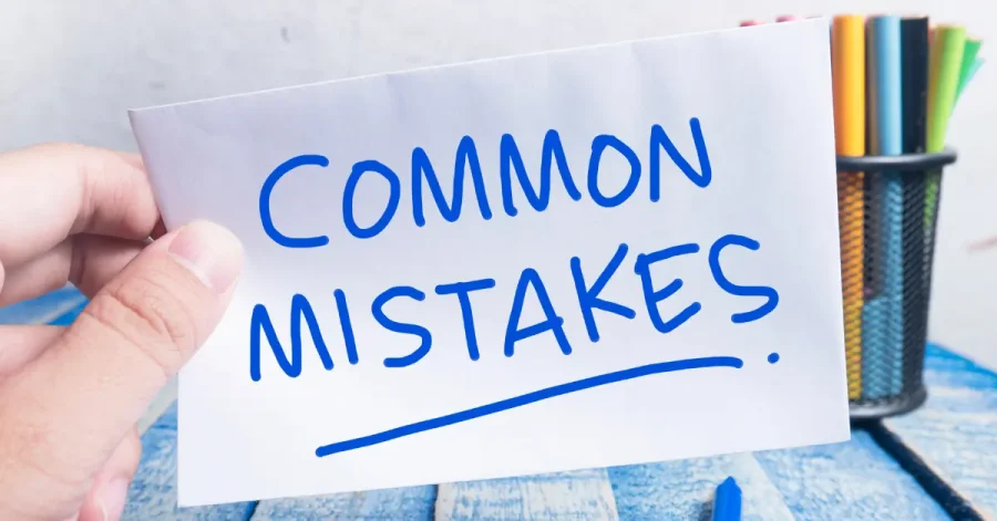 A hand holding a paper with the words "COMMON MISTAKES" written in bold blue marker, with colored pencils in a holder in the background.