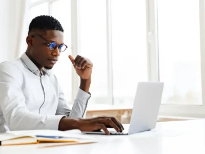 A professional man in a white button-down shirt and glasses studies for the bar exam with Themis + UWorld on a laptop at a bright, modern office desk.