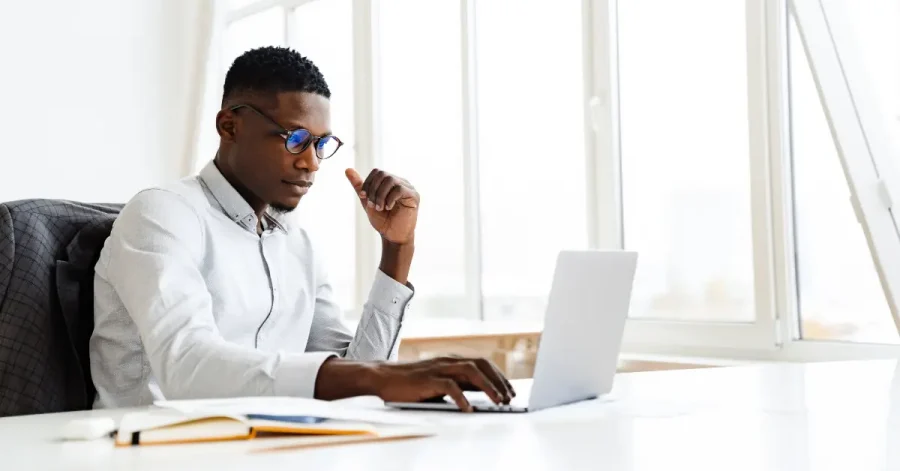 A professional man in a white button-down shirt and glasses studies for the bar exam with Themis + UWorld on a laptop at a bright, modern office desk.
