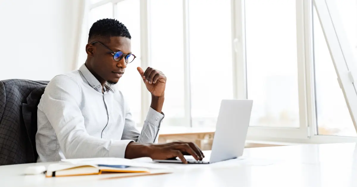 A professional man in a white button-down shirt and glasses studies for the bar exam with Themis + UWorld on a laptop at a bright, modern office desk.