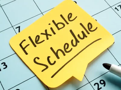 Yellow sticky note with the words "Flexible Schedule" placed on a calendar, next to a black marker.