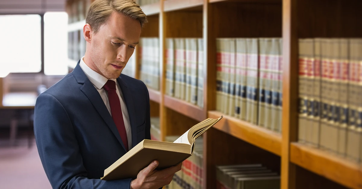 A determined man in a suit reviewing a law book in a library—symbolizing focused preparation for retaking the bar exam